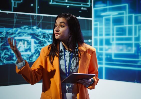 Public speaker doing presentation at tech forum event, explore ways emerging AI technologies can positively enhance companies workforce. Indian woman promoting artificial intelligence solutions